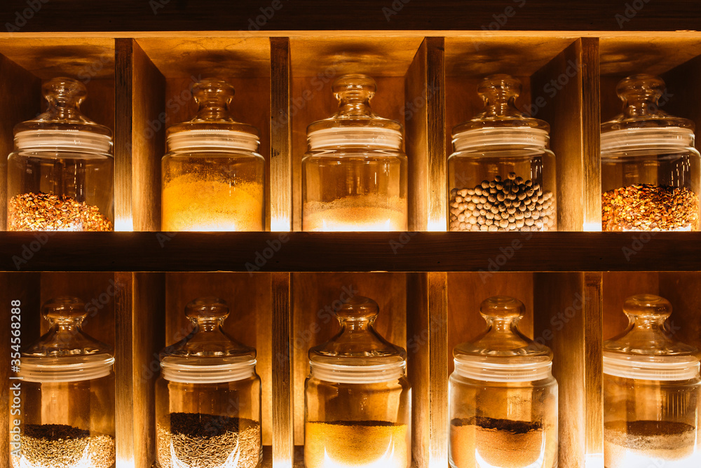 Decorative glass jars with spices on the kitchen shelf. Warm tint