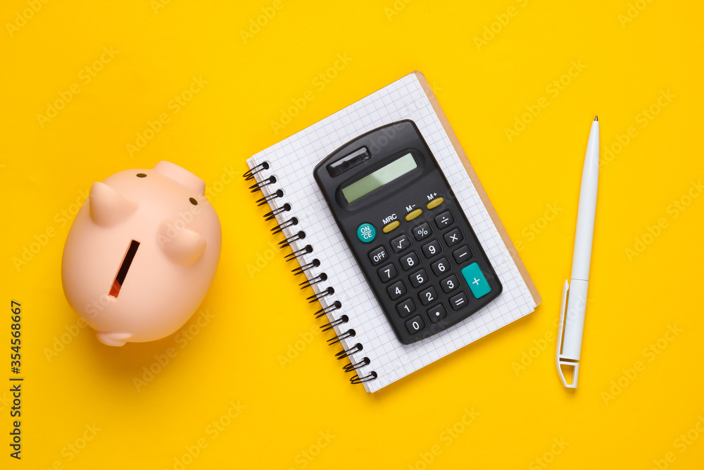 Piggy bank, notebook and calculator on yellow background. Minimalistic studio shot. Overhead view. Flat lay. Piggy bank, notebook and calculator on yellow background. Minimalistic studio shot. Overhead view. Flat lay.