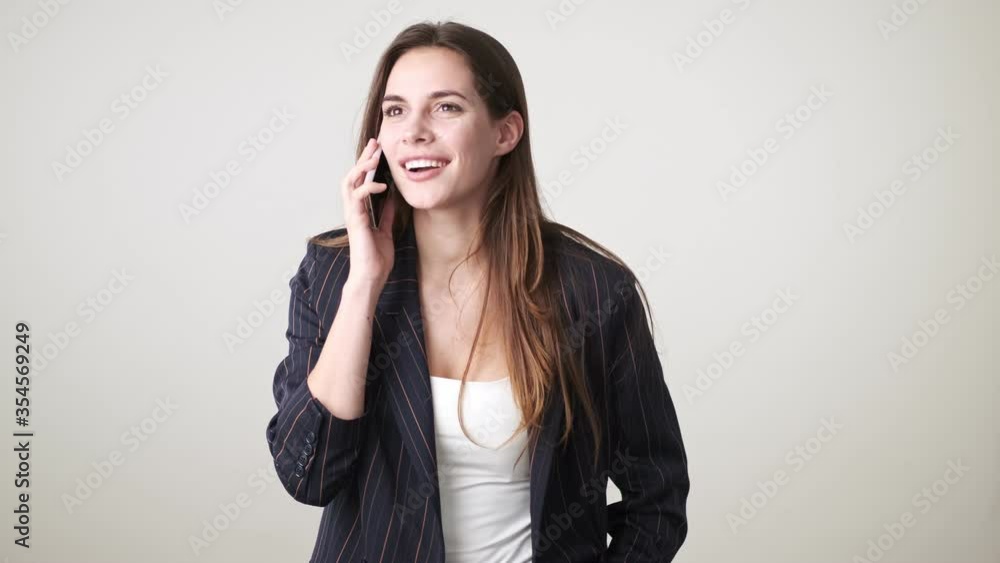 A happy pleased young woman wearing casual clothes is talking on the phone standing isolated over white background in studio A happy pleased young woman wearing casual clothes is talking on the phone standing isolated over white background in studio