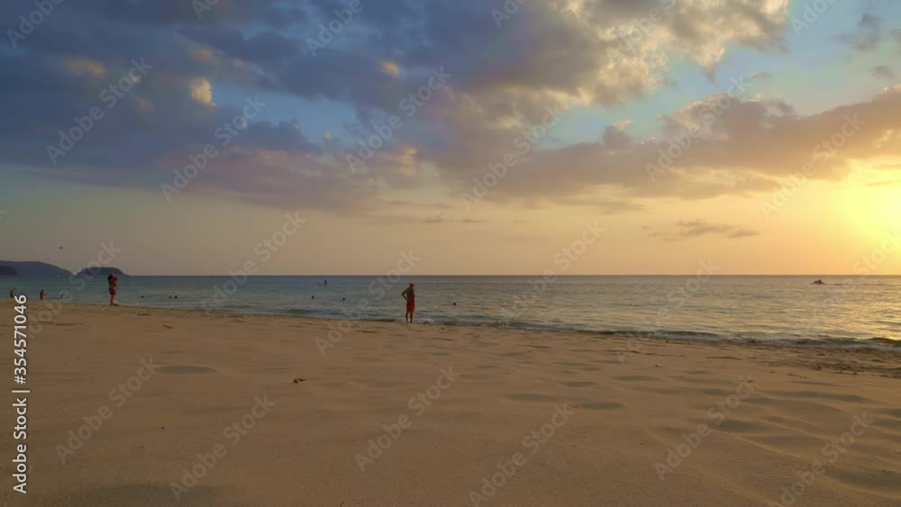 Sunset beach with colorful blue sky and people are walking and swimming in warm tropical ocean with jet ski and yellow sun in background Sunset beach with colorful blue sky and people are walking and swimming in warm tropical ocean with jet ski and yellow sun in background