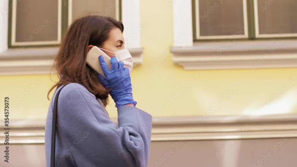health, safety and pandemic concept - young woman in protective medical mask and gloves calling on smartphone and walking along city street health, safety and pandemic concept - young woman in protective medical mask and gloves calling on smartphone and walking along city street