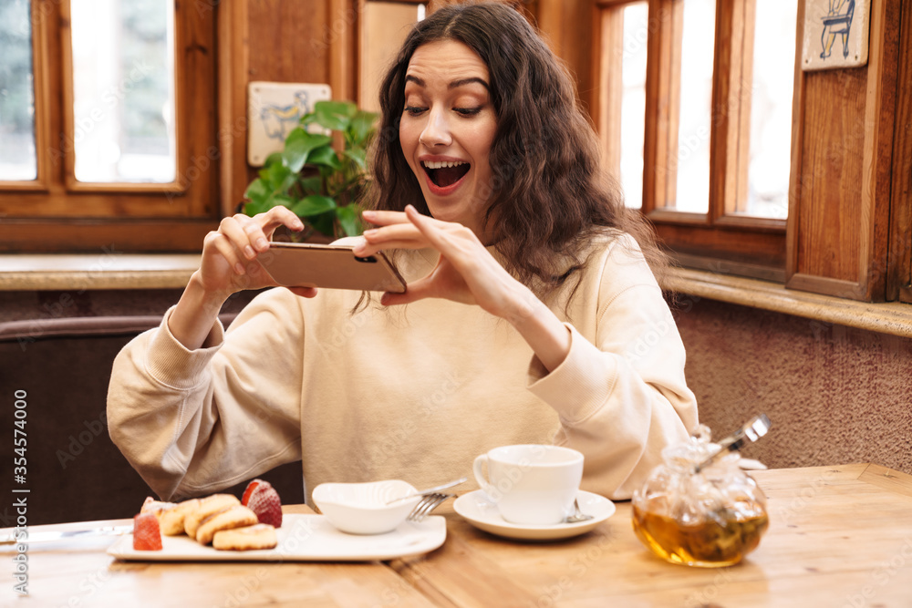 © Drobot Dean - Image of excited woman taking photo on cellphone while having breakfast