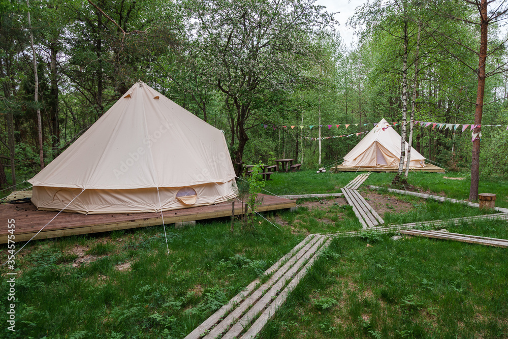 Two glamping camp tents and wooden nature boardwalk in spring green forest of Pleshcheyevo Ozero National Park