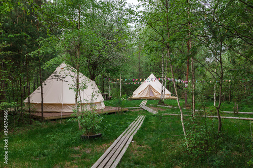 Glamping camp tents on a wooden floor and nature boardwalk in spring green forest of Pleshcheyevo Ozero National Park