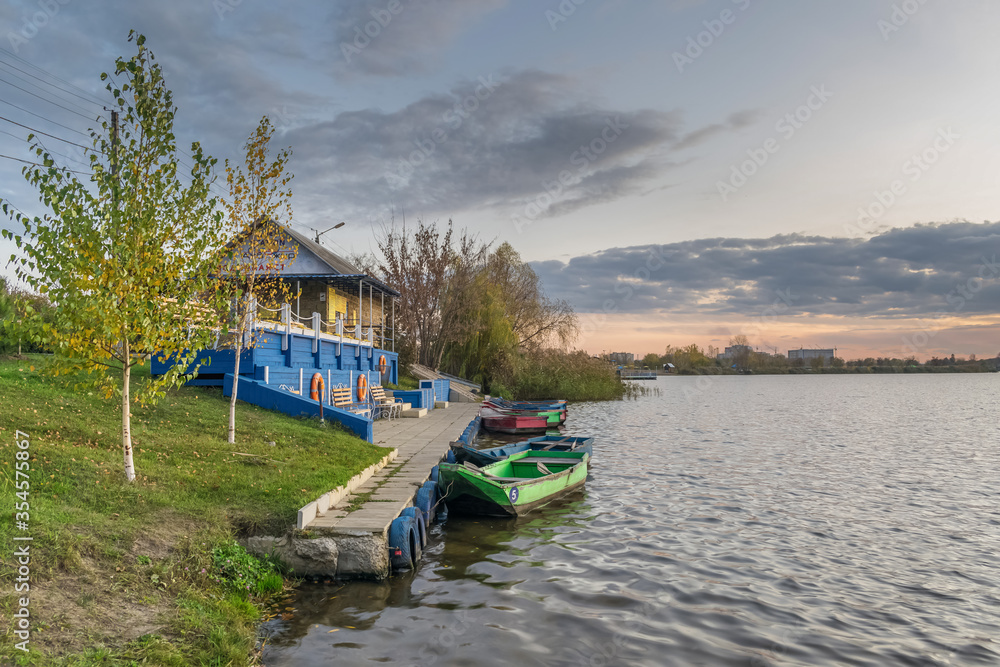 Fototapeta premium Evening landscape near the water with a beautiful sunset and boats near the pier in the Zhuravlevsky Godropark of Kharkov