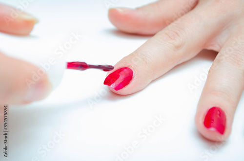 Manicure at home. DIY manicure. The girl paints herself nails in red  burgundy. Glossy nail polish. Macro in macro. Brush is applying varnish on the nail in a strong large zoom on a white background