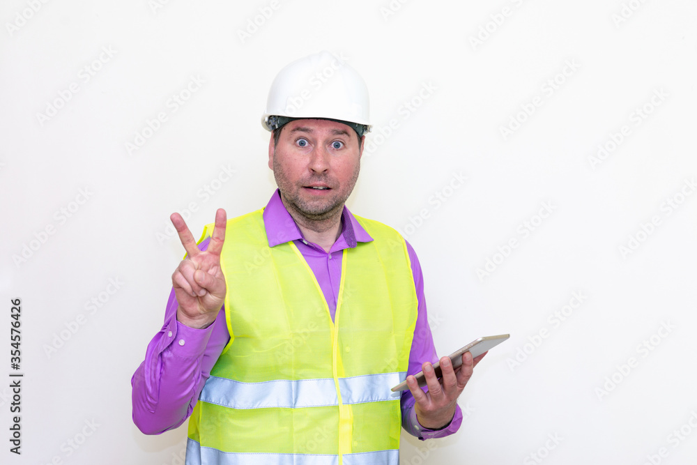 Construction builder wearing helmet yellow protective vest using wireless tablet and showing like or thumbs-up shocked poke up shows to you and victory gesture isolated on white background. Construction builder wearing helmet yellow protective vest using wireless tablet and showing like or thumbs-up shocked poke up shows to you and victory gesture isolated on white background.