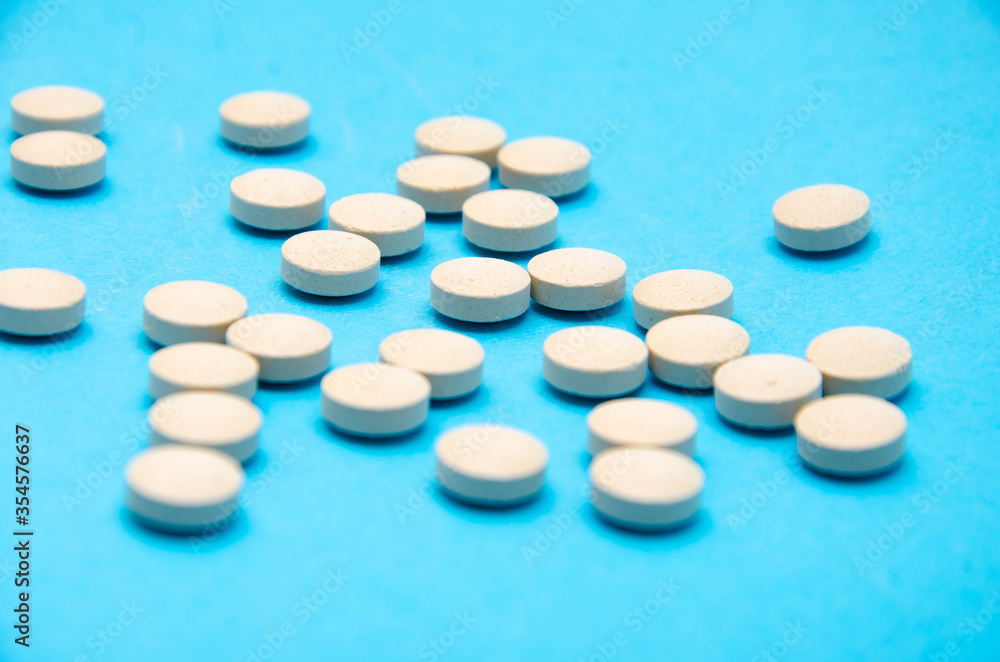 Round white, yellow pills on a blue background top view, side view in macro. Place for text. The tablets lie chaotically on the right, on the left in the middle. Pills in macro Round white, yellow pills on a blue background top view, side view in macro. Place for text. The tablets lie chaotically on the right, on the left in the middle. Pills in macro