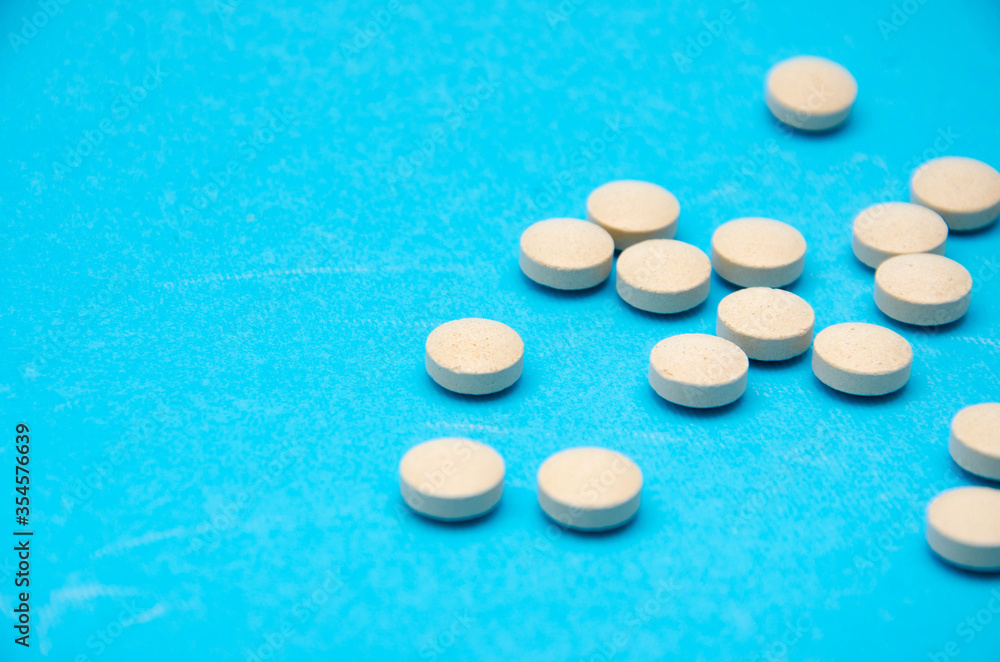 Round white, yellow pills on a blue background top view, side view in macro. Place for text. The tablets lie chaotically on the right, on the left in the middle. Pills in macro Round white, yellow pills on a blue background top view, side view in macro. Place for text. The tablets lie chaotically on the right, on the left in the middle. Pills in macro