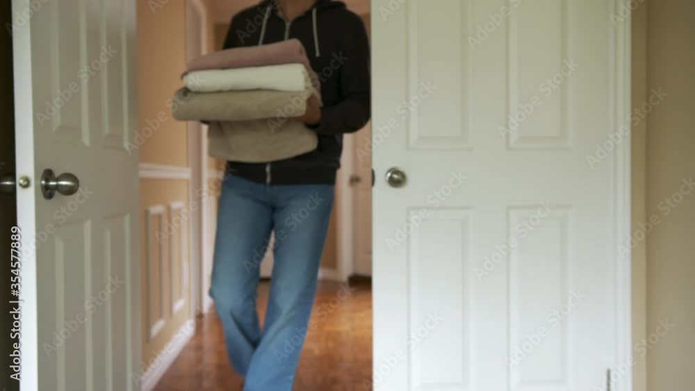 High quality slow motion close-up 4k video of a young man walking into the room on the second floor of his beautiful house and holding bath towels. Young man carrying laundry into the closet High quality slow motion close-up 4k video of a young man walking into the room on the second floor of his beautiful house and holding bath towels. Young man carrying laundry into the closet