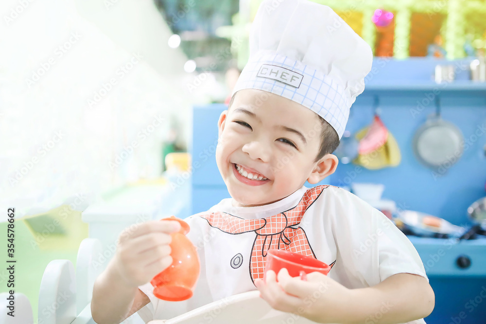 Portrait of cute boy holding teapot in playground with white uniform. little chefs cook in the kitchen Portrait of cute boy holding teapot in playground with white uniform. little chefs cook in the kitchen