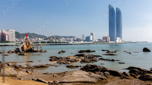 Panorama of Xiamen with twin skyscrapers. A lighthouse and rocks in the foreground. photo