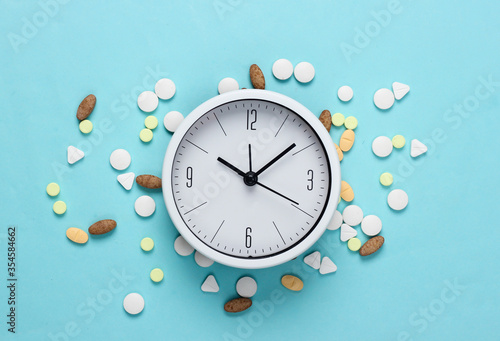 Time to take pills. White clock with pills on blue pastel background. Top view. Flat lay