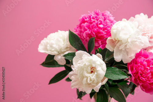 white and pink peonies in a vase against a pink background