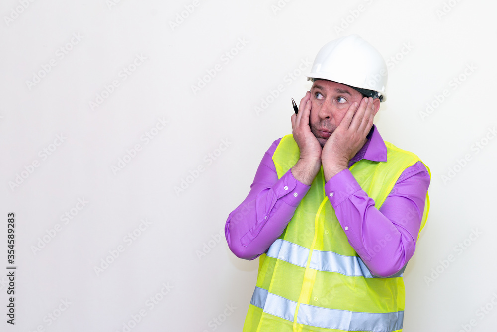 Portrait middle age of caucasian worker wearing hard hat holding pen makes all kinds of grimaces on white studio background. Portrait middle age of caucasian worker wearing hard hat holding pen makes all kinds of grimaces on white studio background.