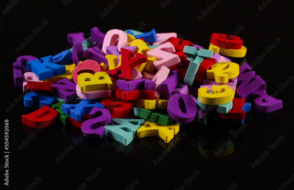 Fototapeta premium Many colored wooden letters isolated on black background.