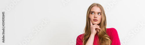 panoramic crop of pensive young woman touching face and looking away isolated on white