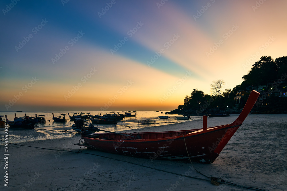 Fantastic sunset with sun light rays on tropical island and boats on beach