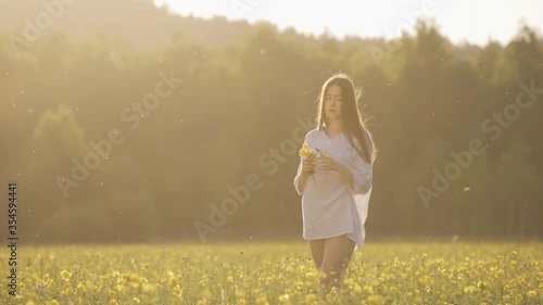 Young woman happy walking through a field and touching yellow flowers.