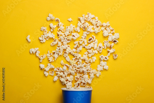 Movie time. Cardboard bucket of popcorn on yellow background. Top view