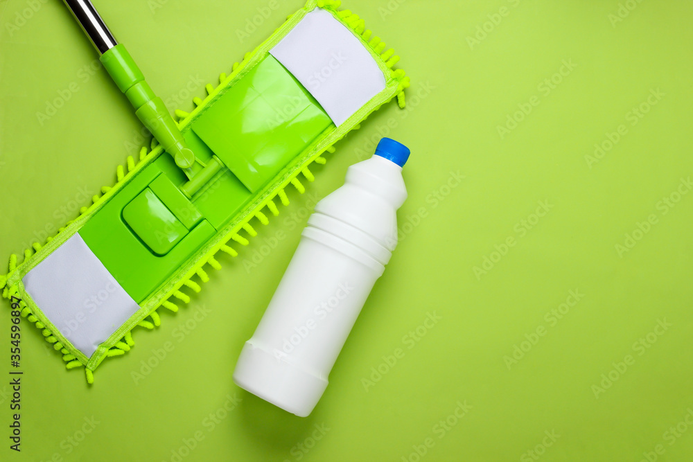 Cleaning products. Plastic mop, bottle of detergent on green background. Disinfection and cleaning in the house. Top view