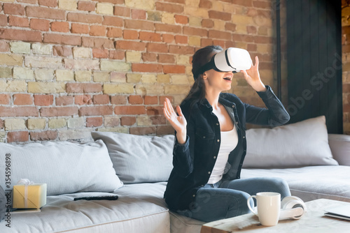 excited woman touching virtual reality headset while sitting on sofa