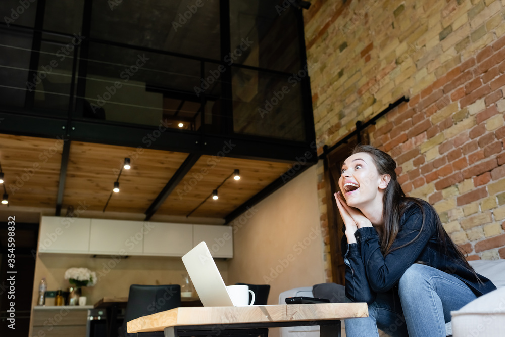 excited girl sitting on sofa and watching movie near laptop and cup excited girl sitting on sofa and watching movie near laptop and cup