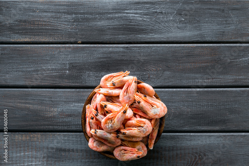 Shrimps in shell in bowl on dark wooden background top-down copy space. Seafood