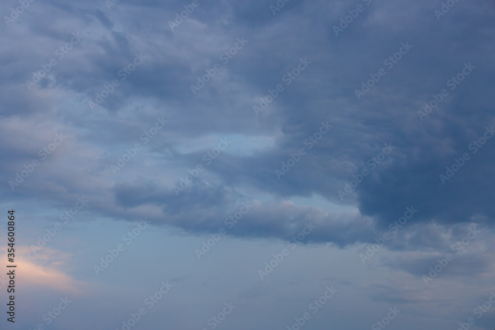Beautiful dramatic gray and white clouds on blue sky, variety of shapes, silhouettes and shades at sunset time