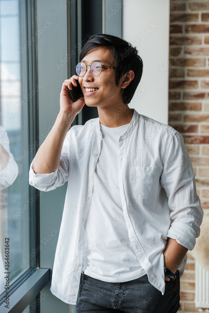 Image of asian man wearing eyeglasses talking on cellphone in office