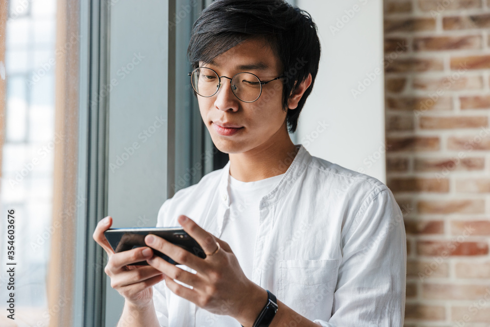 Image of handsome young asian man holding cellphone in office Image of handsome young asian man holding cellphone in office