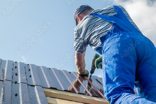 a worker with an electric screwdriver covers the roof with metal sheets