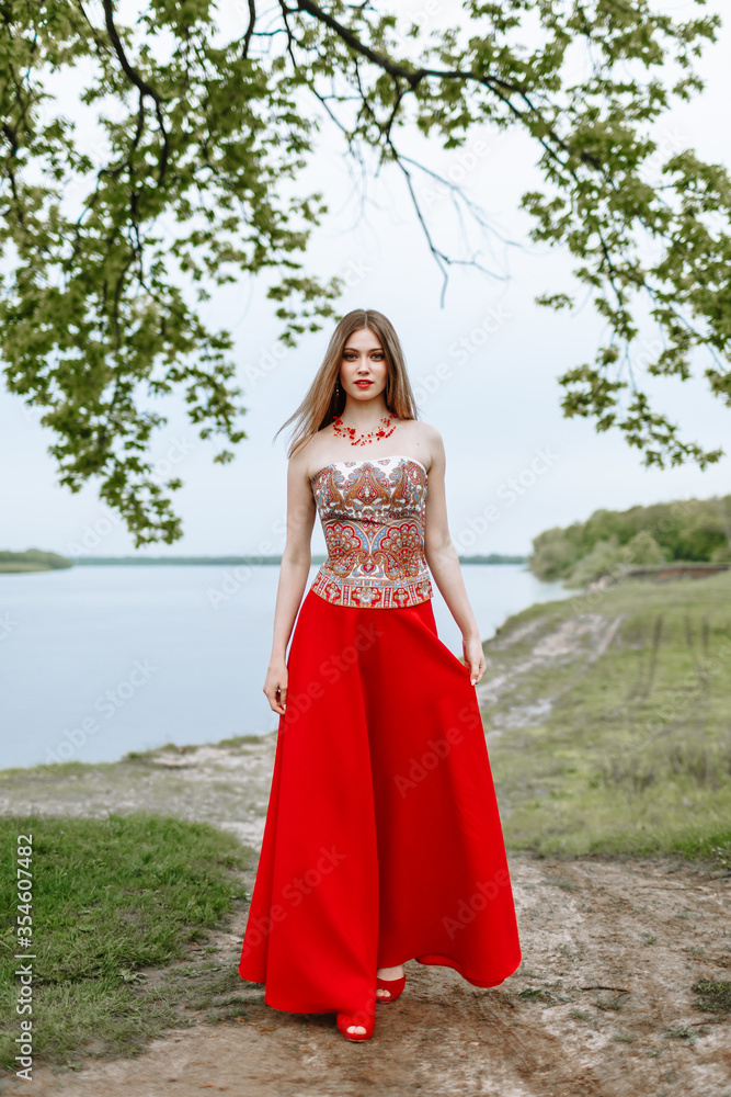 Model in a red dress in nature. Girl on the background of the river Model in a red dress in nature. Girl on the background of the river