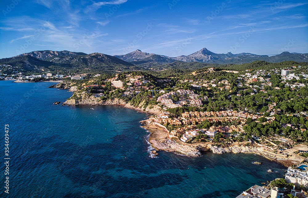 Aerial panorama of Costa de la Calma shoreline and turquoise clear green water of Mediterranean Sea. Hillside villas between pine forests, mountain range in valley. Mallorca, Majorca, Balearic Spain