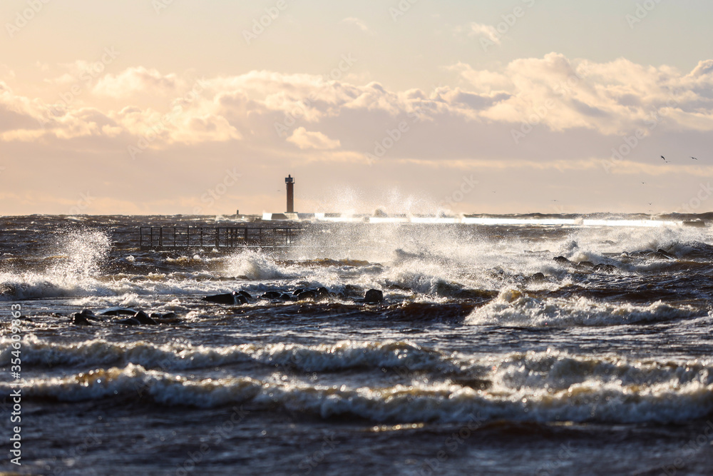 Windy late evening sunset view to Baltic sea lighthouse with large storm waves.