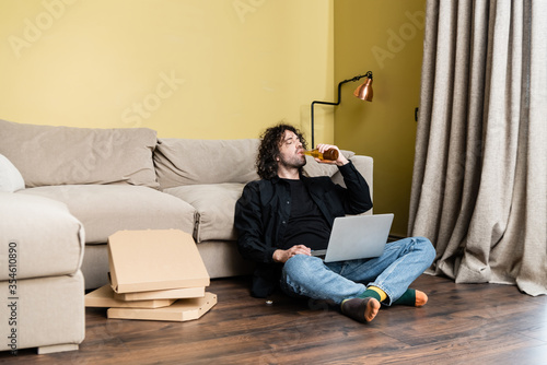 Selective focus of man drinking beer while using laptop near pizza boxes on floor © LIGHTFIELD STUDIOS