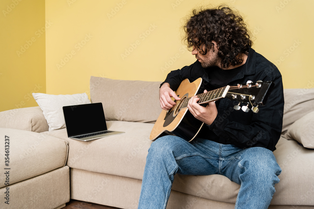 Man playing acoustic guitar during webinar on couch