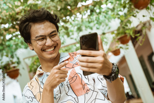 bespectacled youth laughs holding a cellphone when walking