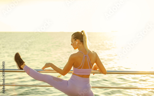 Morning workout. Warming up before training. Young fit woman in sportswear doing leg stretching on the beach at sunrise © splitov27