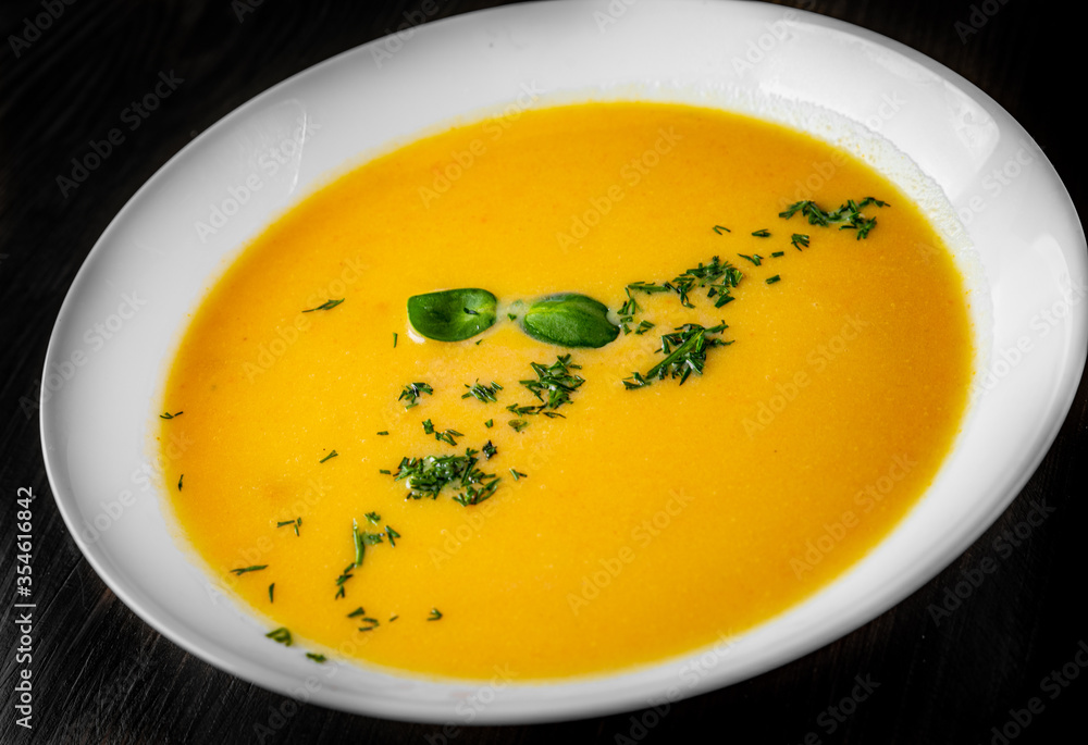 Pumpkin soup in white plate on black wooden table background Pumpkin soup in white plate on black wooden table background