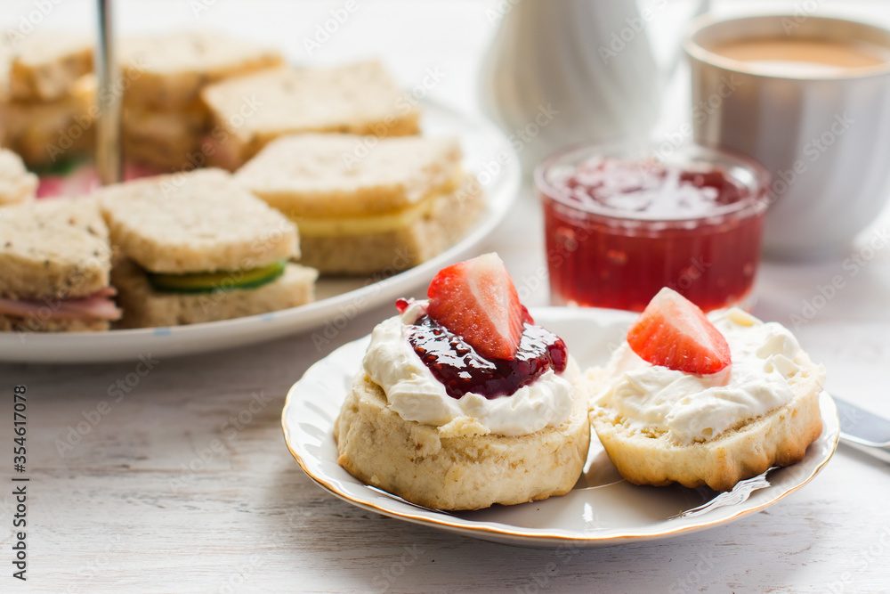 Traditional English afternoon tea: scones with clotted cream and jam, strawberries, with various sadwiches on the background, selective focus