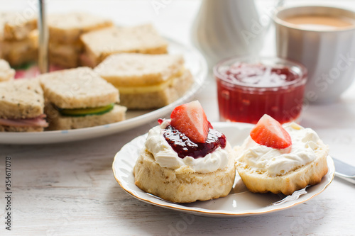 Traditional English afternoon tea: scones with clotted cream and jam, strawberries, with various sadwiches on the background, selective focus photo