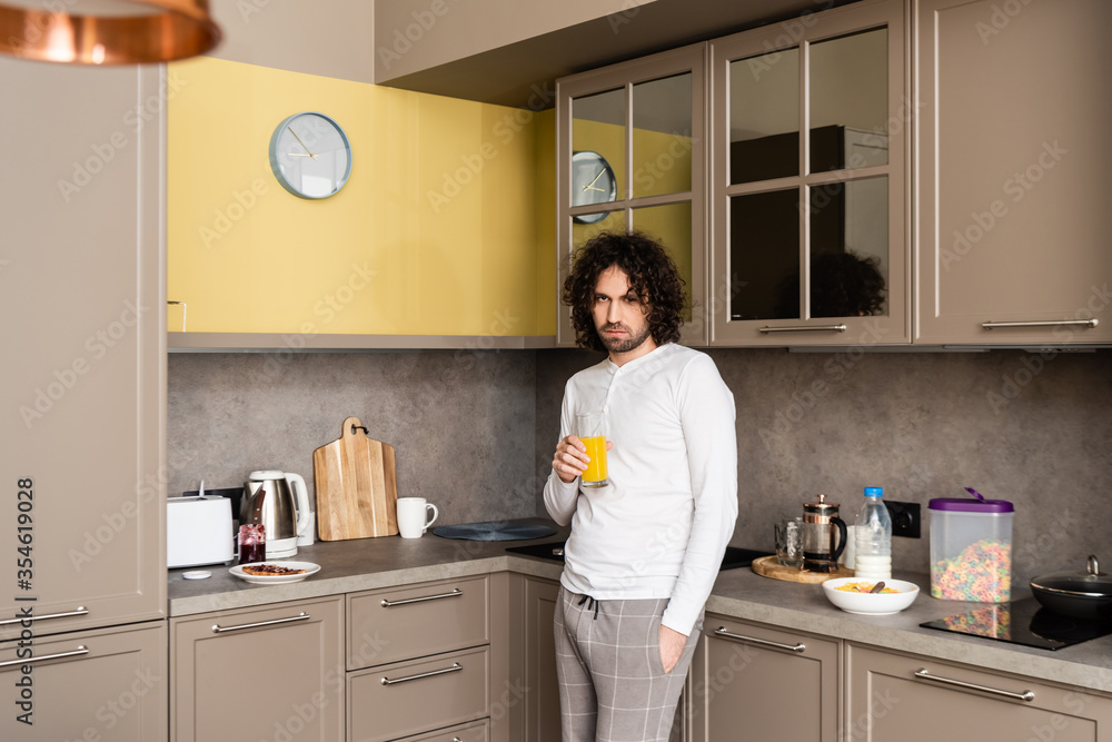 sad man in pajamas looking at camera while holding glass of orange juice in kitchen sad man in pajamas looking at camera while holding glass of orange juice in kitchen