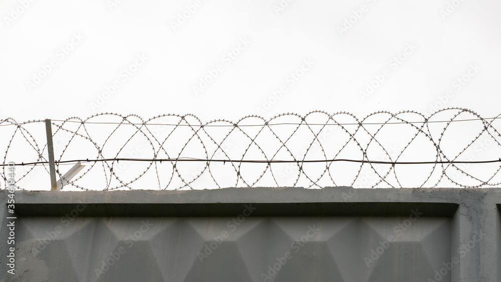 gray concrete wall with barbed wire against the background of a gray nondescript sky gray concrete wall with barbed wire against the background of a gray nondescript sky