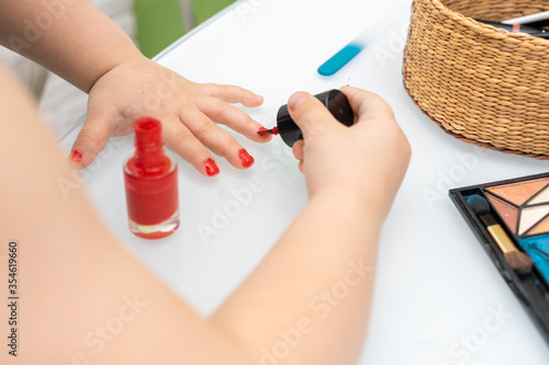 little girl paints nails with red varnish