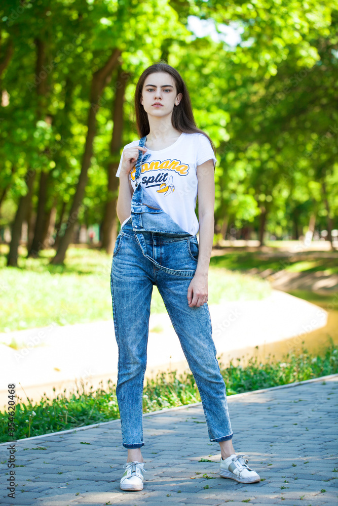 Portrait of a young beautiful teenager girl in blue jeans overalls