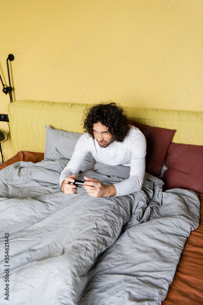 Fototapeta premium KYIV, UKRAINE - APRIL 25, 2020: high angle view of concentrated young man playing video game in bed