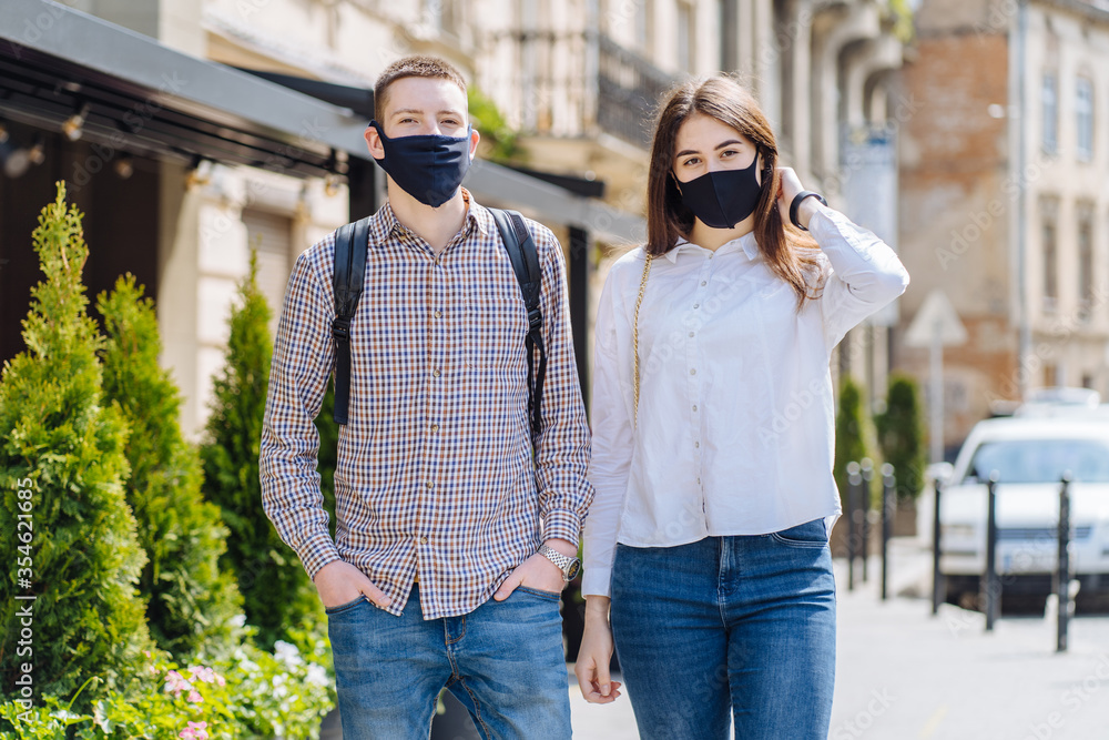 Couple in protective masks have a walk outdoors in the city near business building at quarantine time. Conception of coronavirus pandemic.