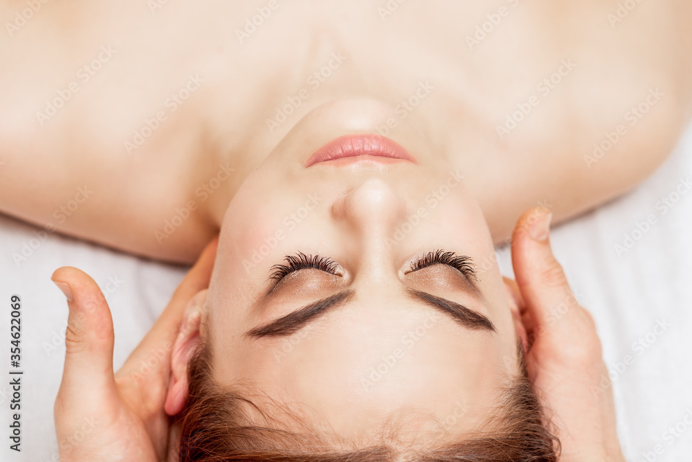 Top view of beautiful young woman having head massage in spa salon.