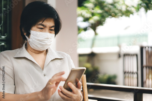 Asian elderly woman wear mask protect virus at outdoor and using smart phone for internet.